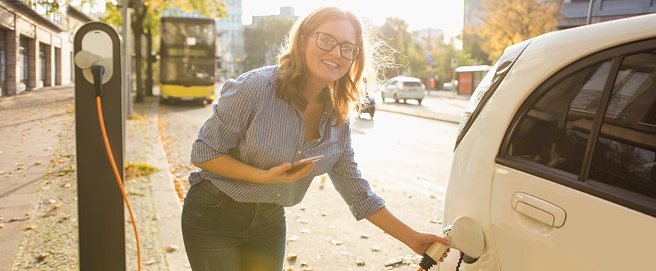 Frau mit Handy in der Hand lädt ein E-Auto